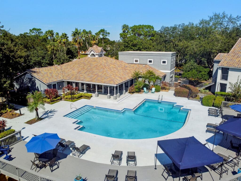 Dog-Friendly Luxury Apartments In East Orlando, FL - Pine Harbour - Resort-Inspired Pool With Sundeck, Lounge Tanning Chairs, Tables, Chairs, And Umbrellas.